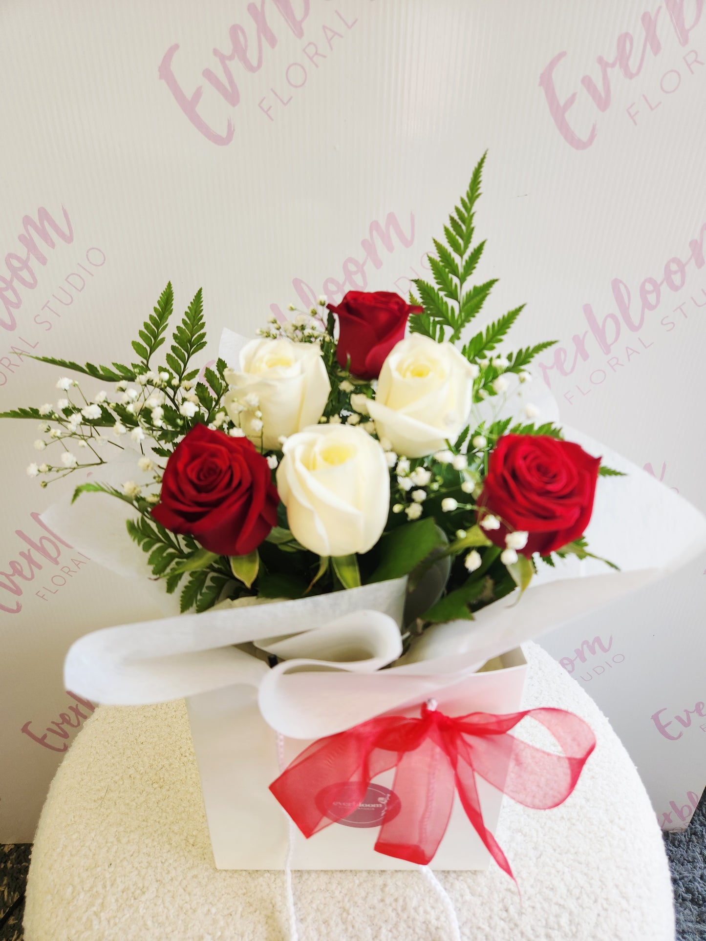 Red and white rose bouquet wrapped in soft white paper in flower bag with red bow. Tauranga Florist - Everbloom floral studio