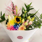 Fresh seasonal flower bouquet in bright mixed flowers wrapped in white paper and dressed with a bow.