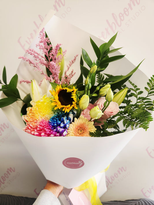 Fresh seasonal flower bouquet in bright mixed flowers wrapped in white paper and dressed with a bow.