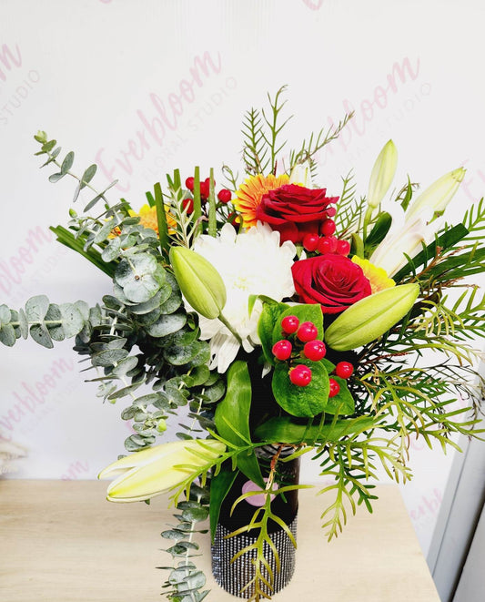 A beautifully arranged Christmas bouquet of flowers including red and white roses, lilies, and other holiday-seasonal flowers.