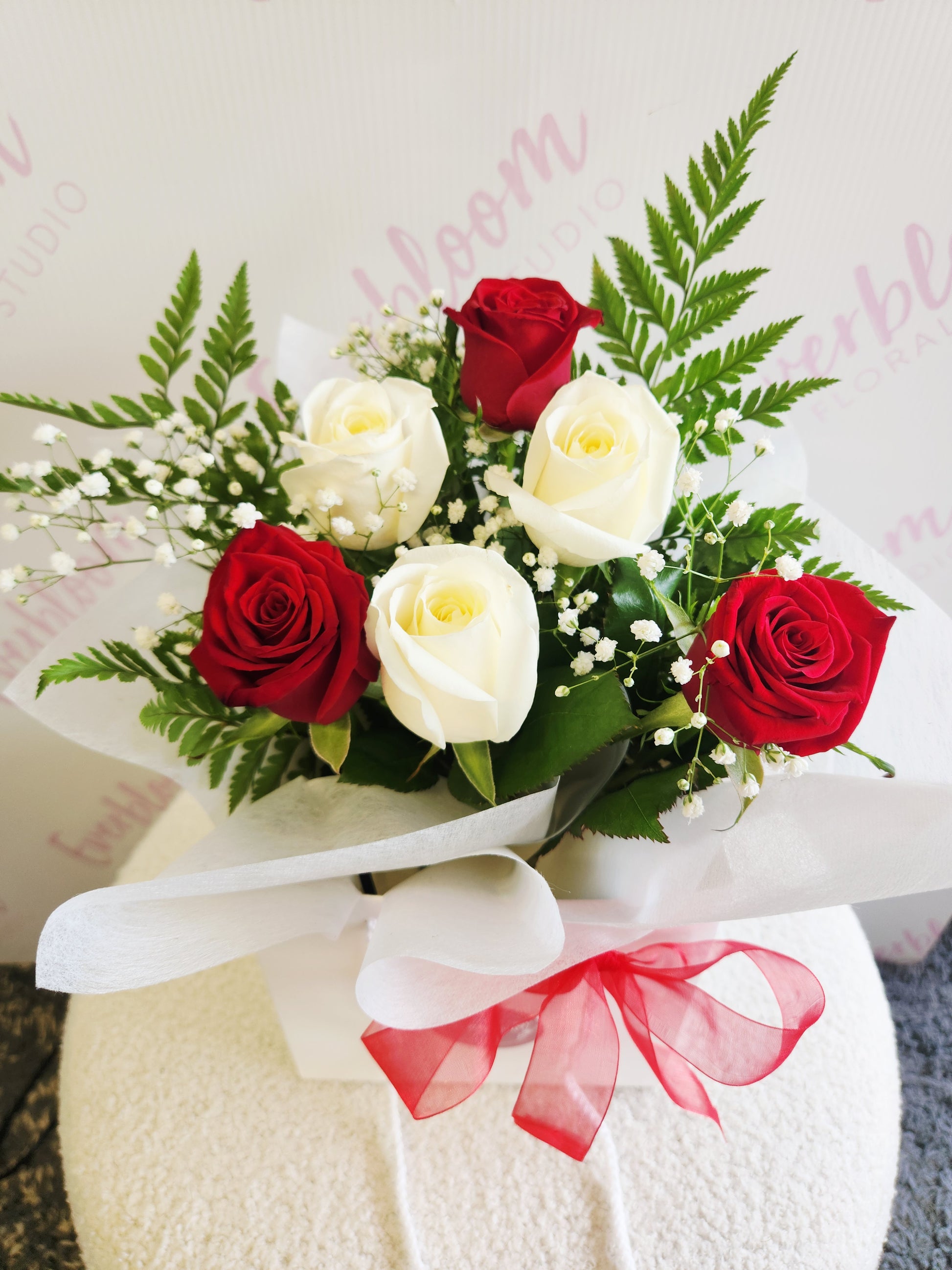 Red and white rose bouquet wrapped in soft white paper in flower bag with red bow. Tauranga Florist - Everbloom floral studio