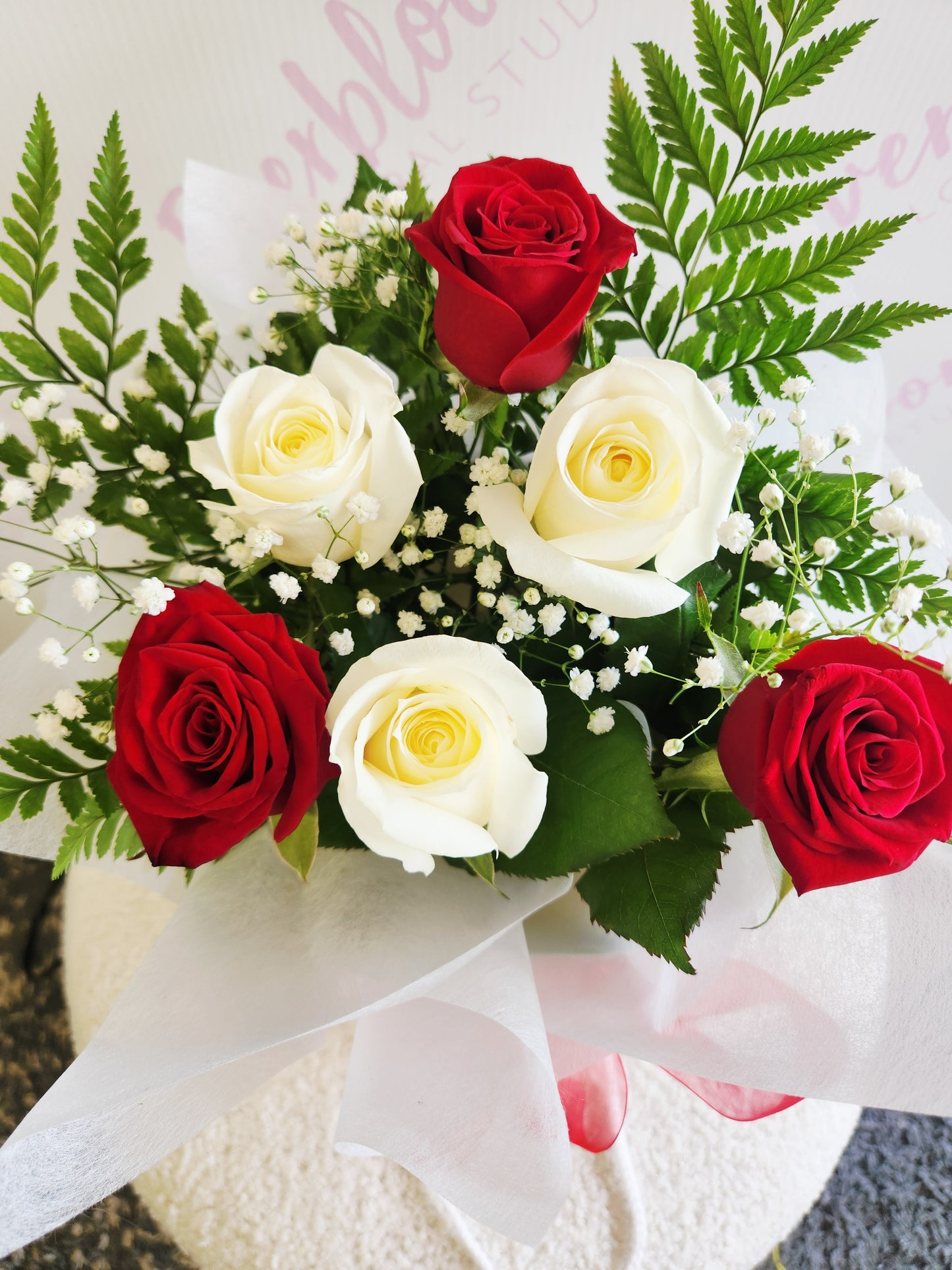 Red and white rose bouquet wrapped in soft white paper in flower bag with red bow. Tauranga Florist - Everbloom floral studio